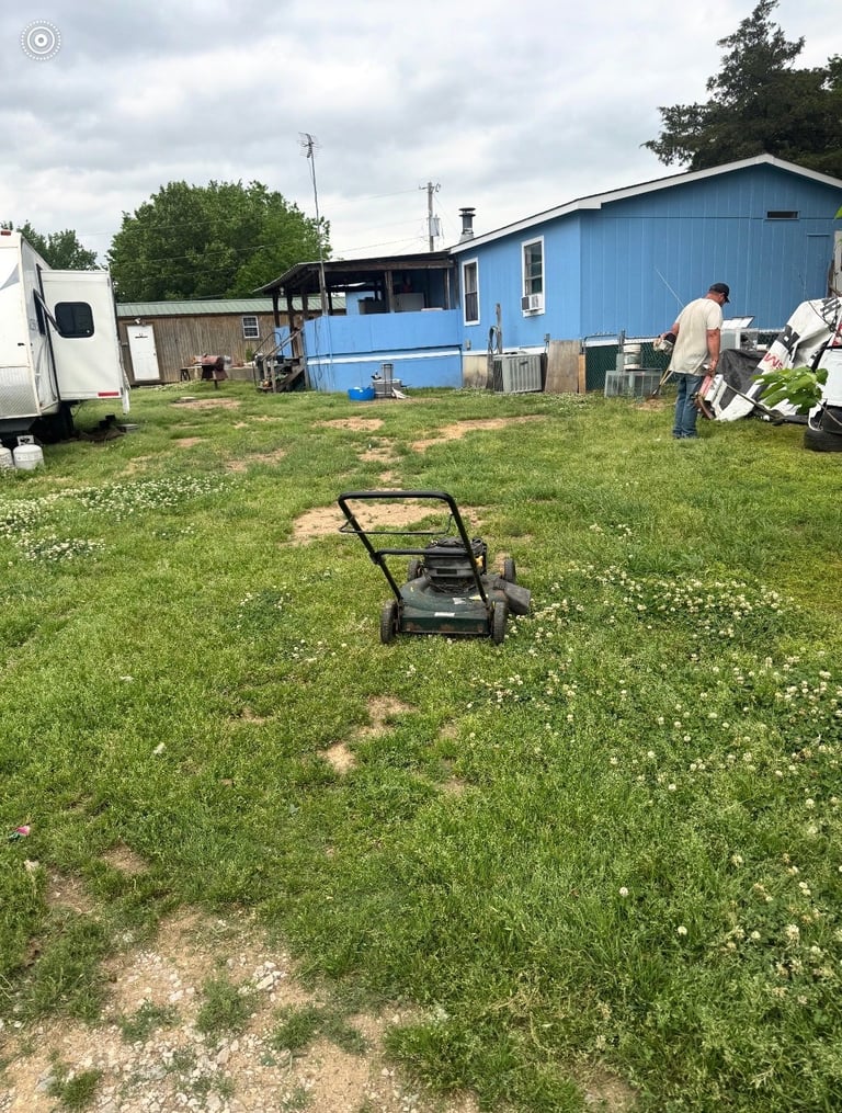 Lawn mower on grass with blue mobile home and white trailer in background