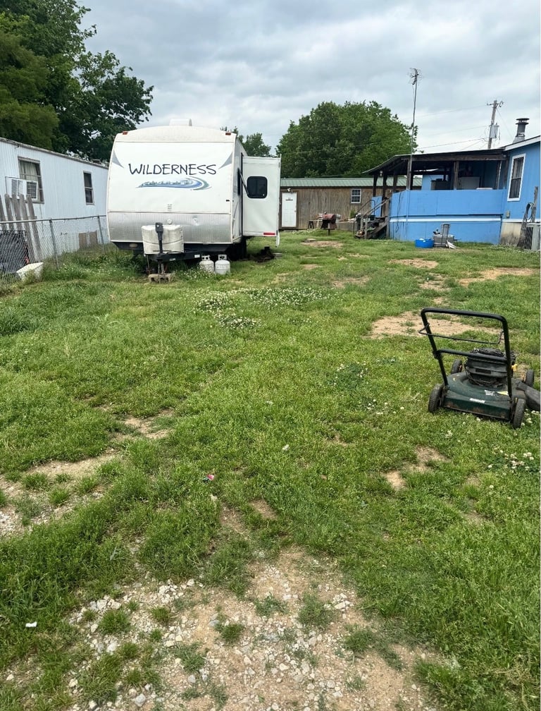 White Wilderness travel trailer parked in a grassy lot with mobile homes and a lawn mower in the foreground